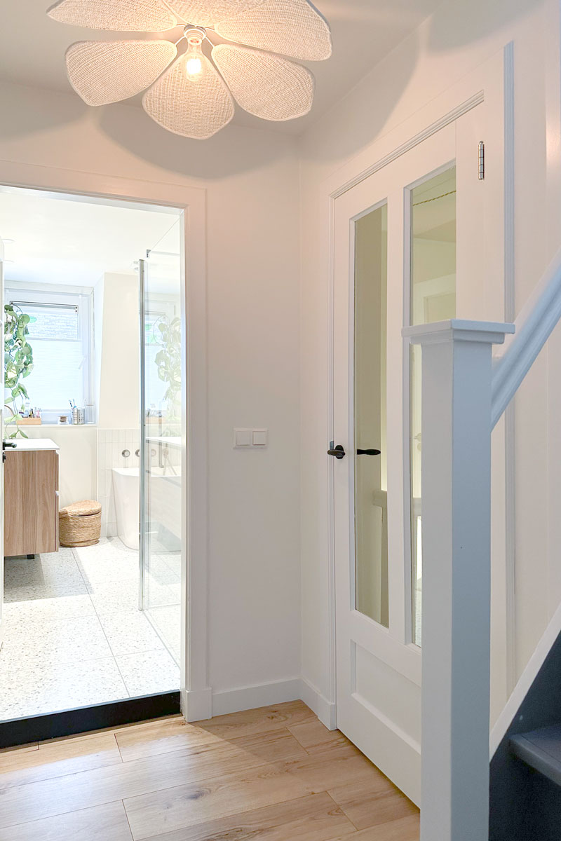 Ingang naar moderne badkamer in jaren 30 woning met houten wastafelmeubel en terrazzo vloer.
